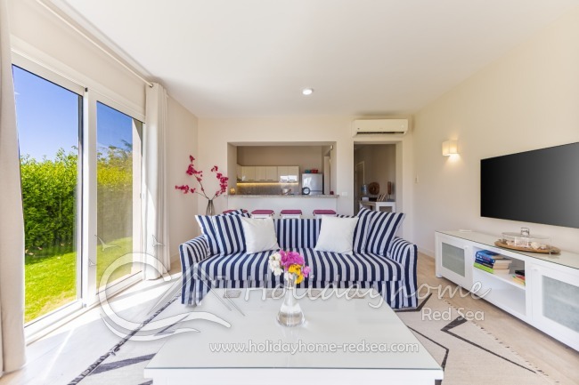 Wohnzimmer mit großem Fernseher, offener Küche und Theke als Essbereich