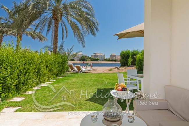 Terrasse und Garten mit Sitzkissen, Esstisch, Sonnenschirm und Sonnenliegen im Garten 